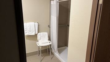 A bathroom with a shower, a white chair, and two towels hanging on the wall.