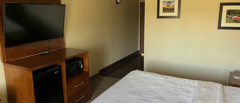 A hotel room with a large bed, a flat-screen TV, a wooden cabinet, and a microwave.
