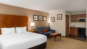 A hotel room with a large bed, a blue sofa, a small table, a desk, a lamp, a microwave, and a kitchenette. - Wingate by Wyndham Clearfield (Clearfield)