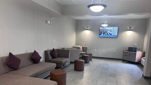 A modern lounge area with sofas and ottomans, a flat-screen TV mounted on the wall, and a small desk with a laptop. - Wingate by Wyndham Clearfield (Clearfield)