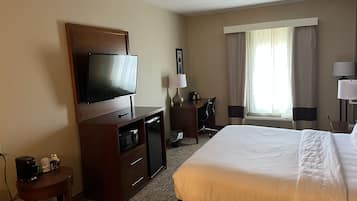 Habitación de hotel con una cama grande, televisión, escritorio con silla y ventana con cortinas.