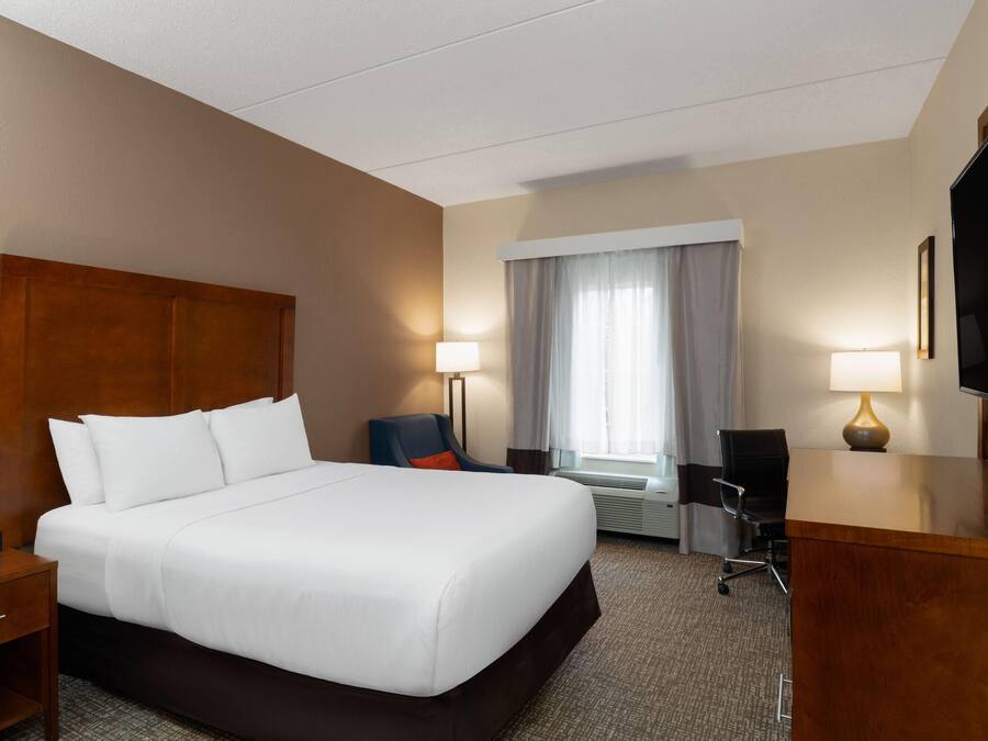 A hotel room with a large bed, a desk, a chair, a TV, and a window with curtains.