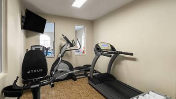 Academia com esteira, elíptica e bicicleta ergométrica, uma televisão e uma janela com vista.