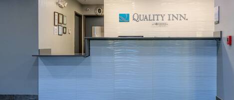 A reception area with a closed sliding door, a reception desk, and a green mat with the hotel name.