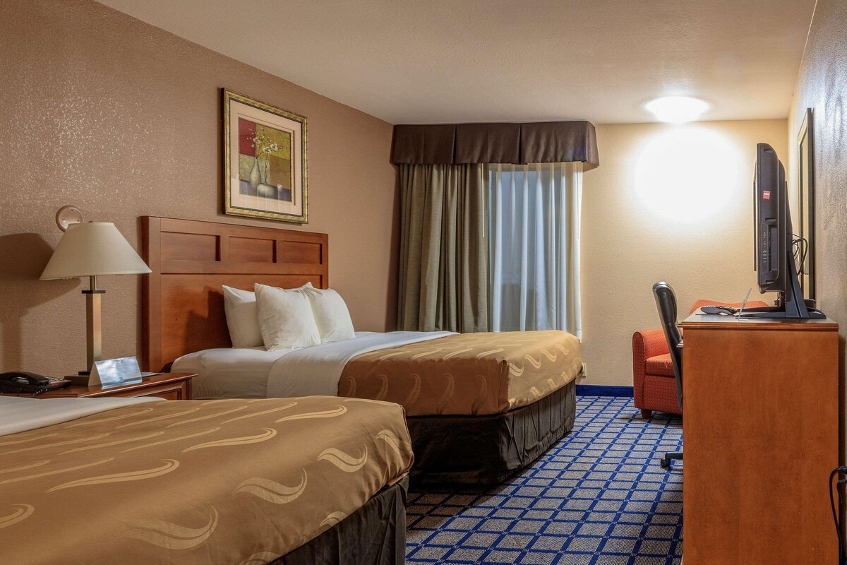 A hotel room with two beds, a desk with a computer, a lamp, and a television.
