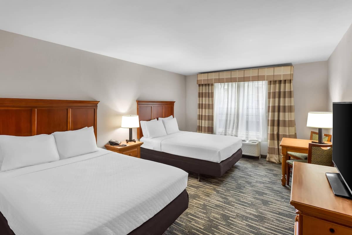 A hotel room with two beds, a desk, a television, and a window with curtains.