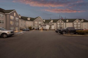 A hotel with a central entrance, multiple floors, and a parking lot with several vehicles.