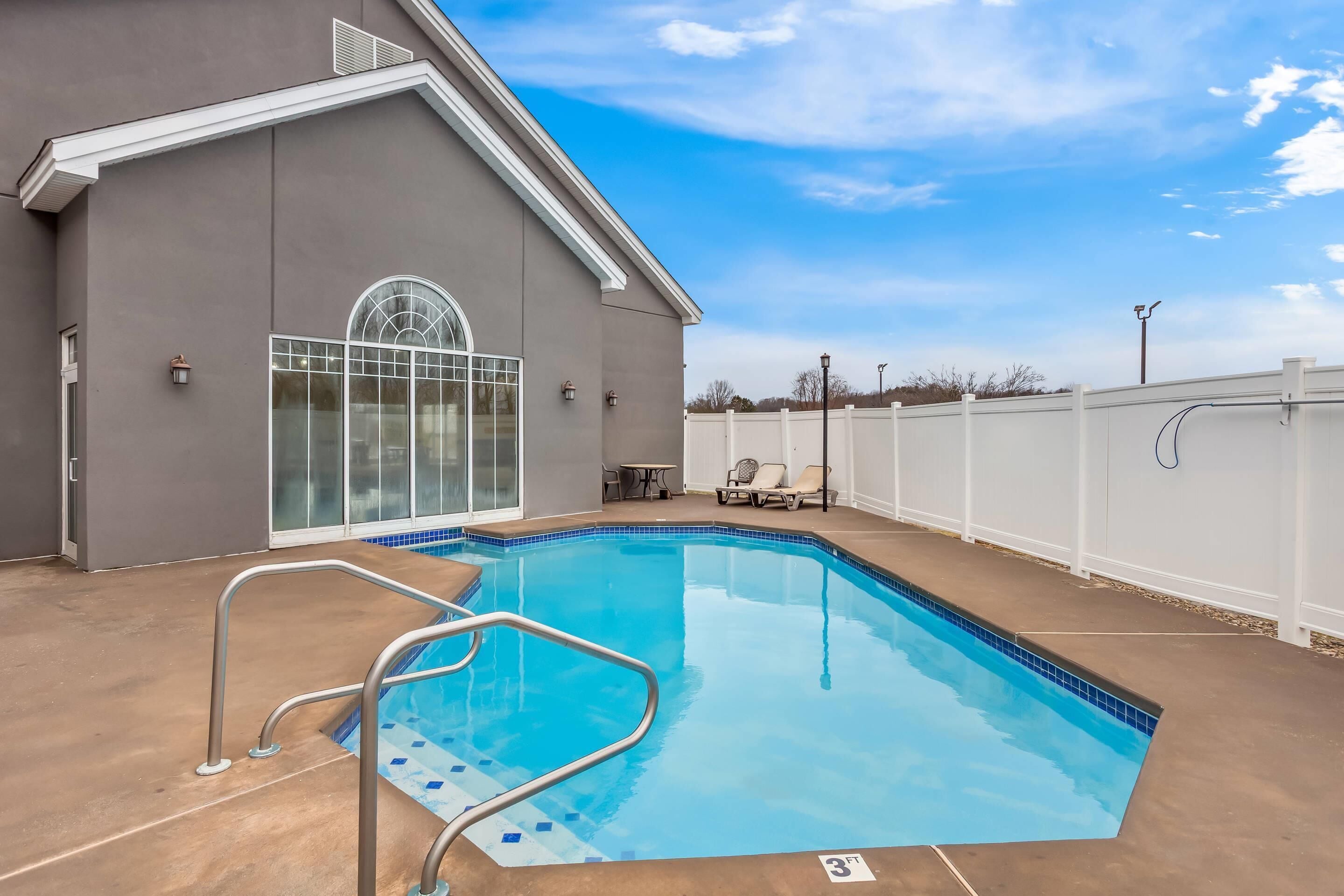 A swimming pool with a metal ladder, a covered patio area, and a white fence in the background.