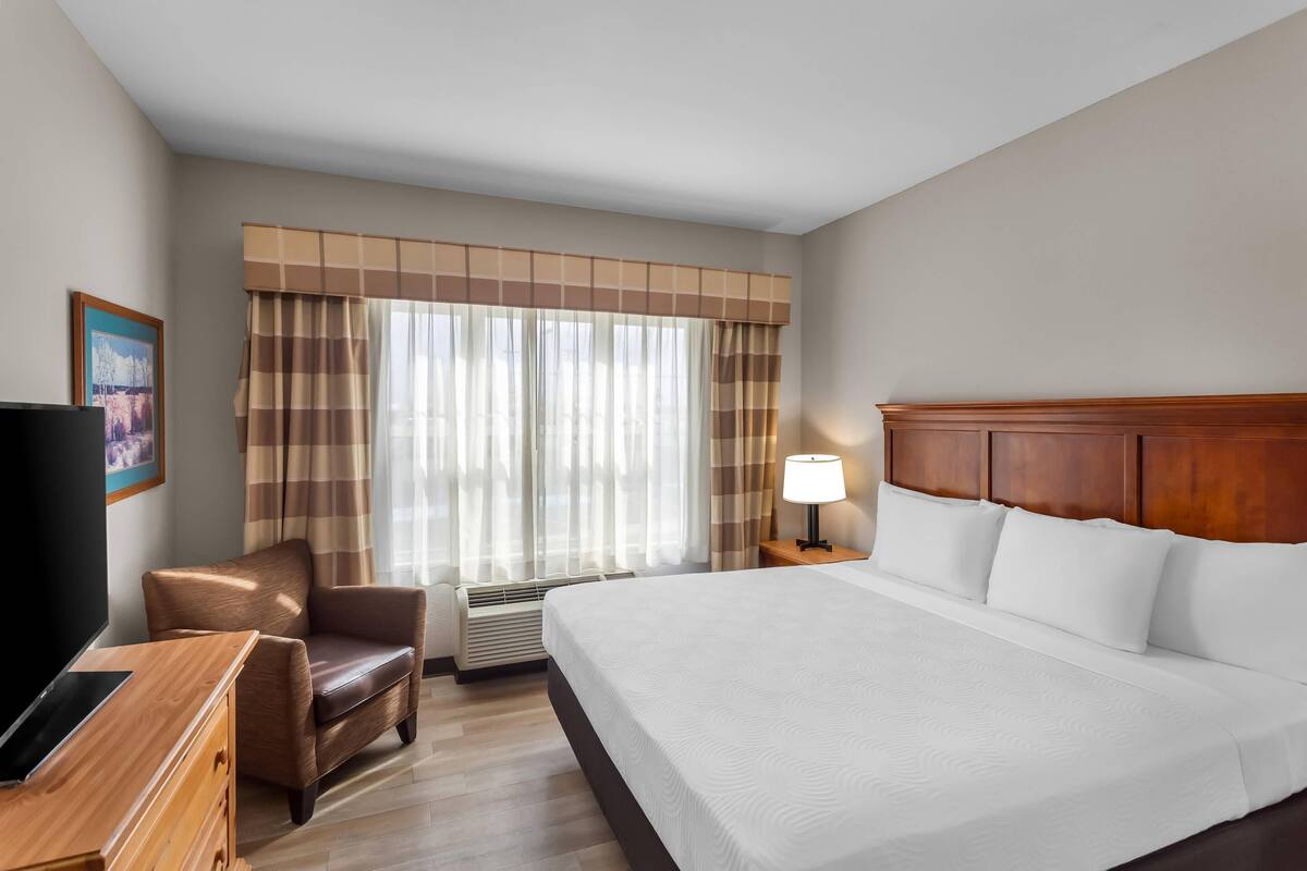A hotel room with a large bed, a desk, a chair, a TV, a lamp, and a window with curtains.