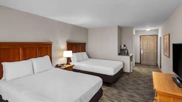 Habitación de hotel con dos camas, un escritorio con lámpara, televisión y puerta que da a un pasillo.