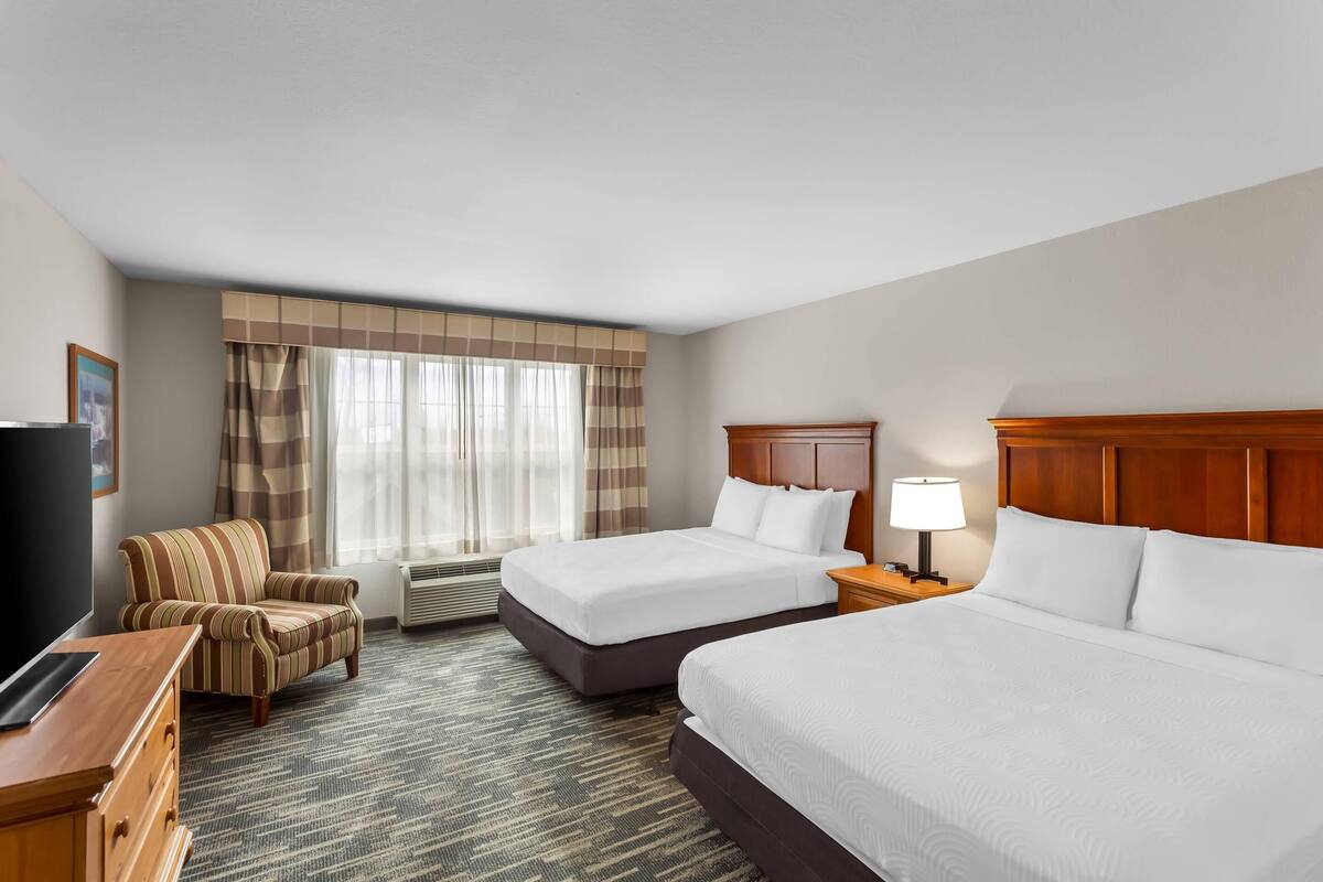 A hotel room with two beds, a desk, a chair, a TV, and a window with curtains.