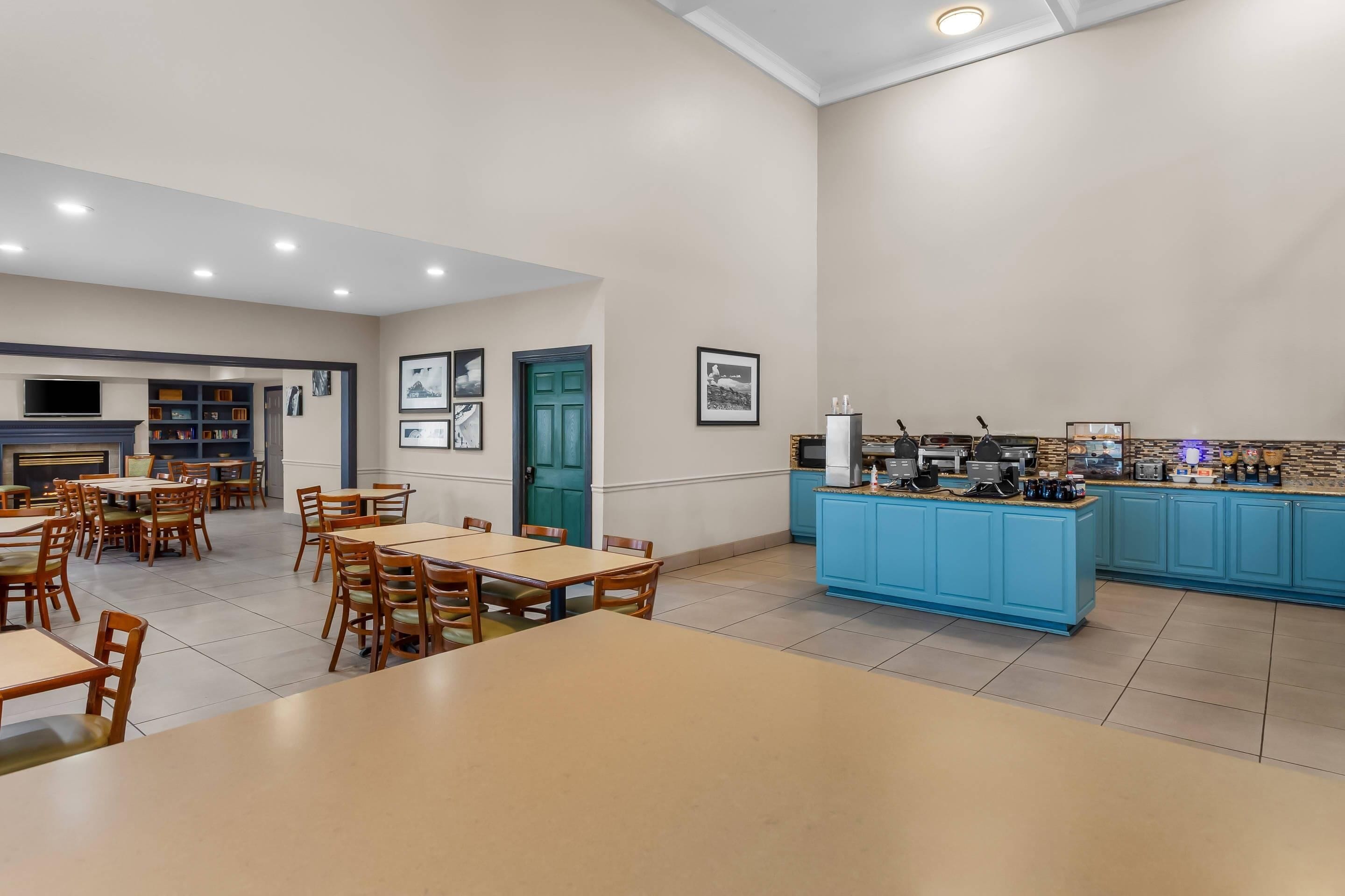 Un comedor amplio con varias mesas y sillas, una zona de cocina con armarios azules y un televisor montado en la pared.