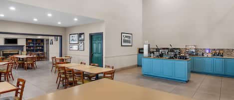 Un comedor amplio con varias mesas y sillas, una zona de cocina con armarios azules y un televisor montado en la pared.