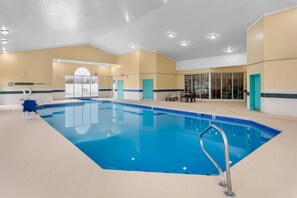 An indoor swimming pool with clear blue water, a pool ladder, and a seating area with chairs and a table.