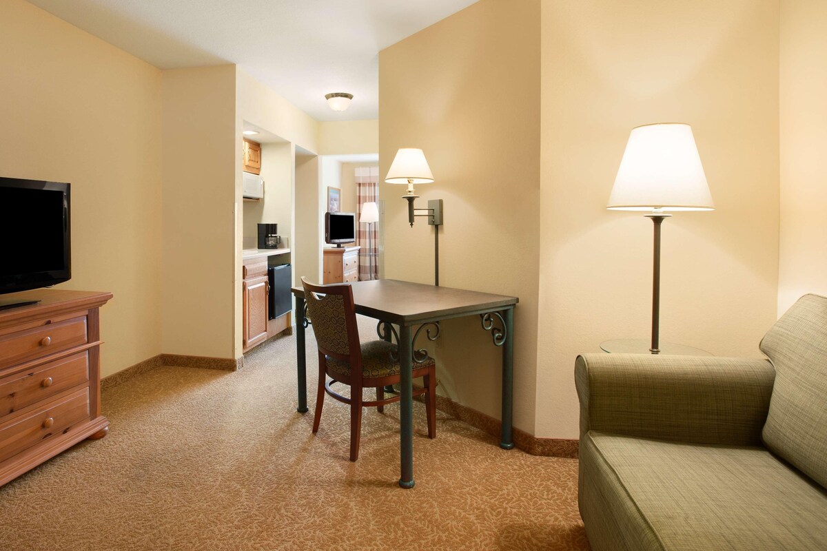 A hotel room with a dining table, a TV, a sofa, and two lamps.