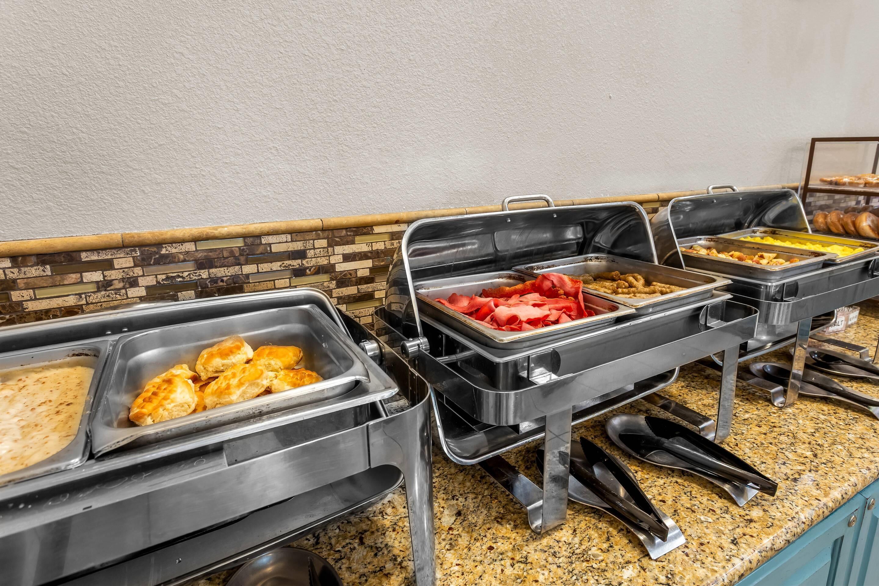 Montaje de bufé con diversos alimentos en bandejas, incluyendo pasteles, frutas y otros platos.