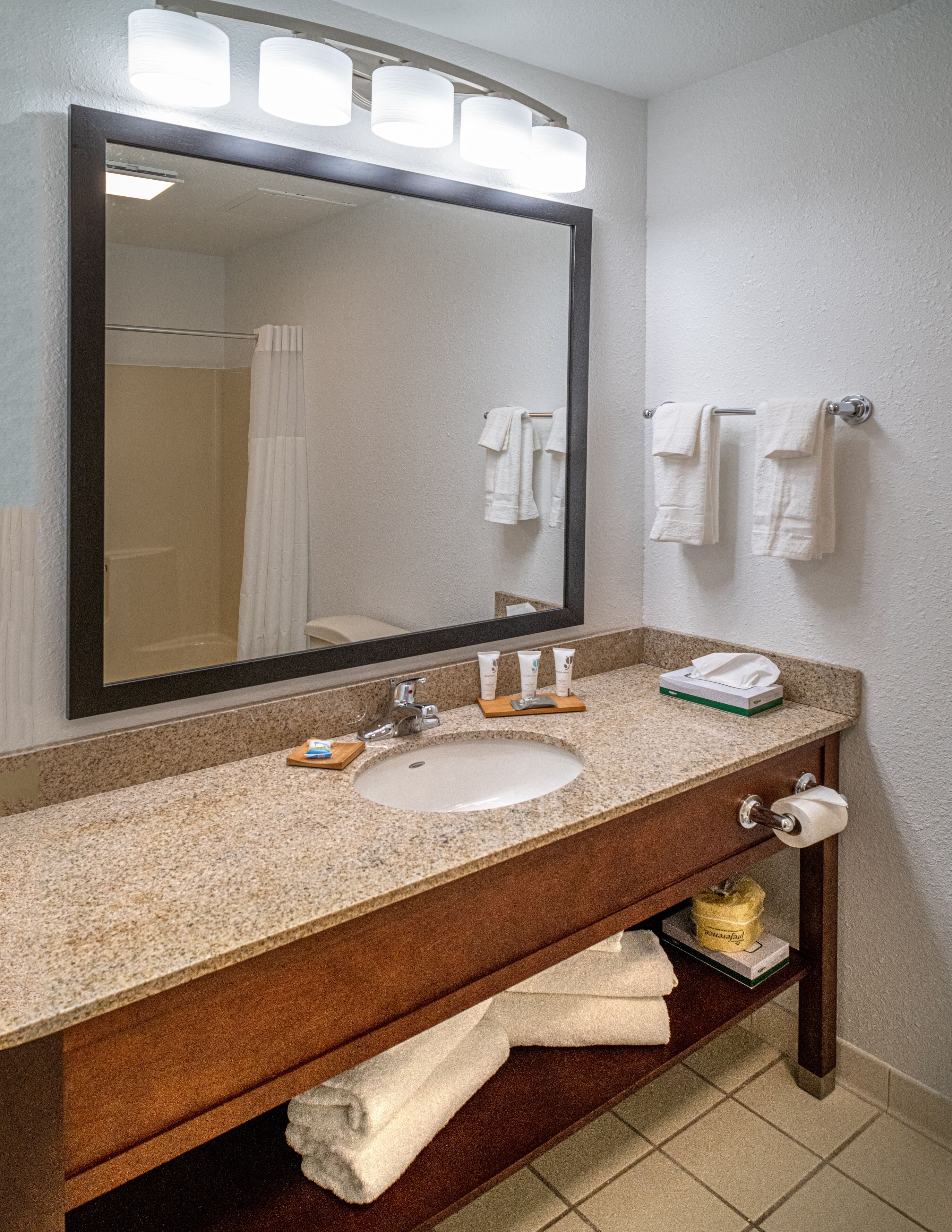 A bathroom with a sink, mirror, towel rack, and a toilet paper holder.