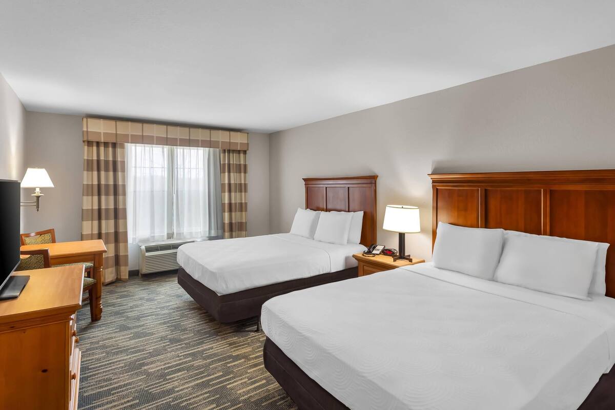 A hotel room with two beds, a desk, a chair, a TV, and a window with curtains.