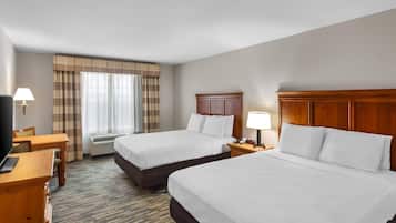 A hotel room with two beds, a desk, a chair, a TV, and a window with curtains.