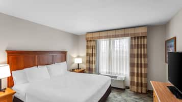 Una habitación de hotel con una cama grande, cabecera de madera, mesita de noche con lámpara, televisor y ventana con cortinas.