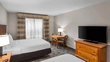 Habitación de hotel con dos camas, televisión, escritorio con lámpara y una silla.