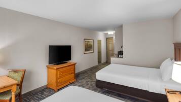 A hotel room with a bed, a television on a wooden dresser, a dining table with chairs, and a carpeted floor.