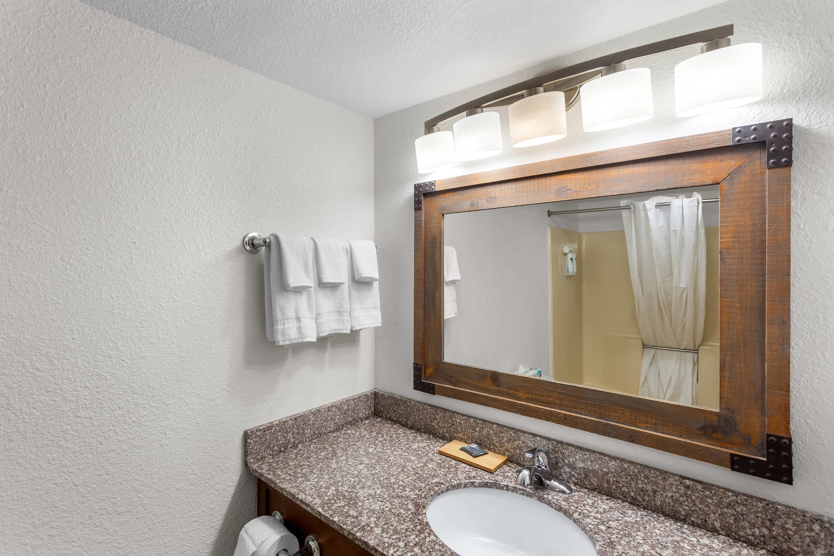 A bathroom with a granite countertop, a white sink, a wooden-framed mirror, and a towel rack with white towels.