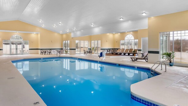 Une piscine intérieure dotée de chaises longues et de tables, entourée de grandes fenêtres et surmontée d’un haut plafond.