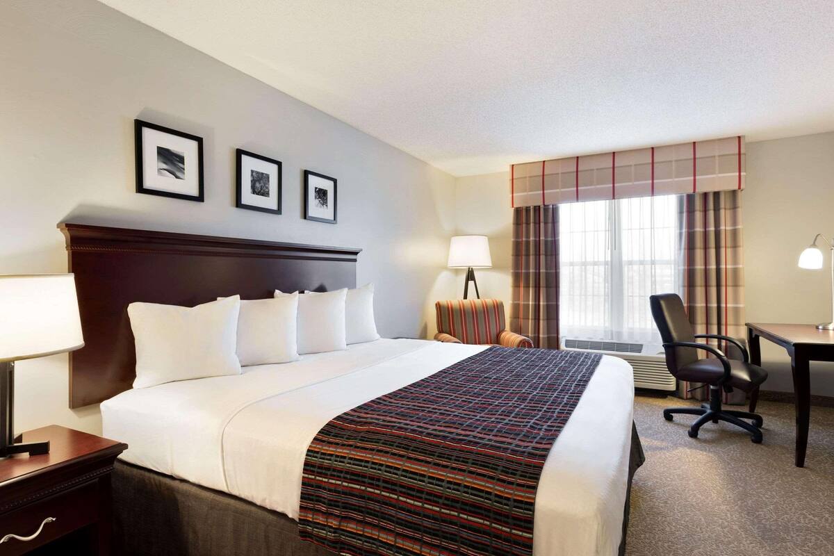 A hotel room with a large bed, a desk, a chair, a lamp, and a window with curtains.