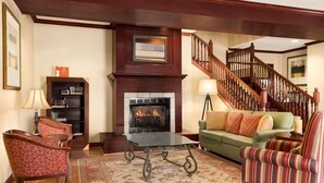 A living room with a fireplace, a staircase, and a green sofa. - Country Inn & Suites by Radisson, Kearney, NE (Kearney)