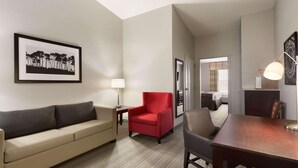 A hotel room with a sofa, a red armchair, a dining table, and a framed picture on the wall. - Country Inn & Suites by Radisson, Kearney, NE (Kearney)