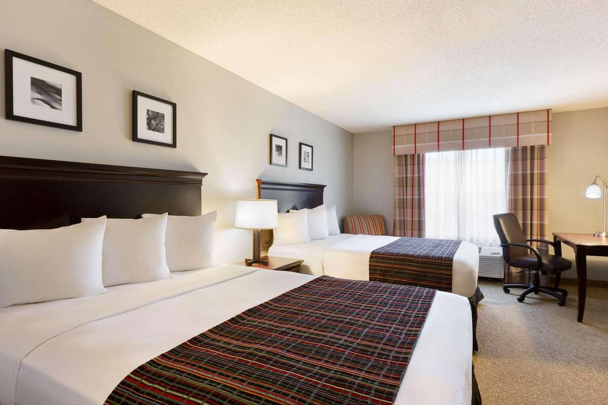 A hotel room with two beds, a desk, a chair, and a window with curtains.