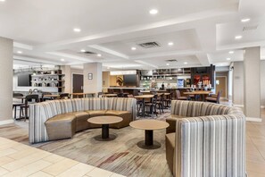 Un moderno vestíbulo de hotel con una zona de estar, un bar y una cocina al fondo.