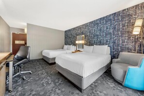 Habitación de hotel con una cama grande, dos mesitas de noche, un escritorio, una silla y una pared con diseño.