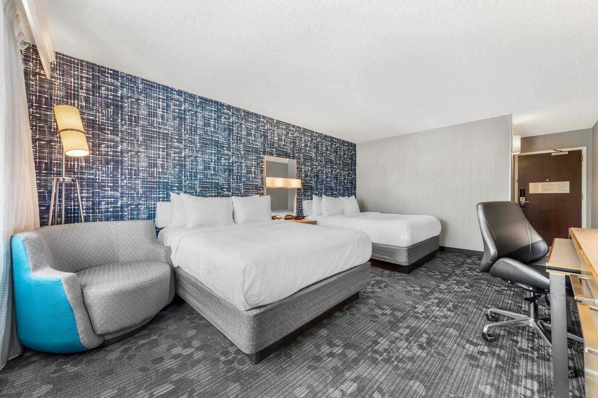 A hotel room with a large bed, two bedside tables, a desk, a chair, and a patterned wall.