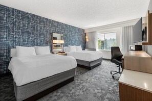 Habitación de hotel con dos camas, un escritorio, un televisor y un ventanal grande.