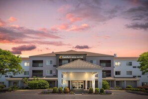 Un hotel de varios pisos con una entrada central, rodeado de vegetación, bajo un cielo al atardecer.