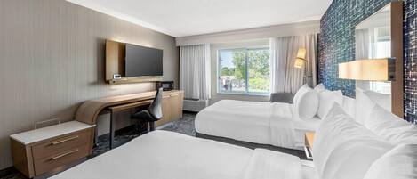 Habitación de hotel con dos camas, un escritorio, un televisor y un ventanal grande.