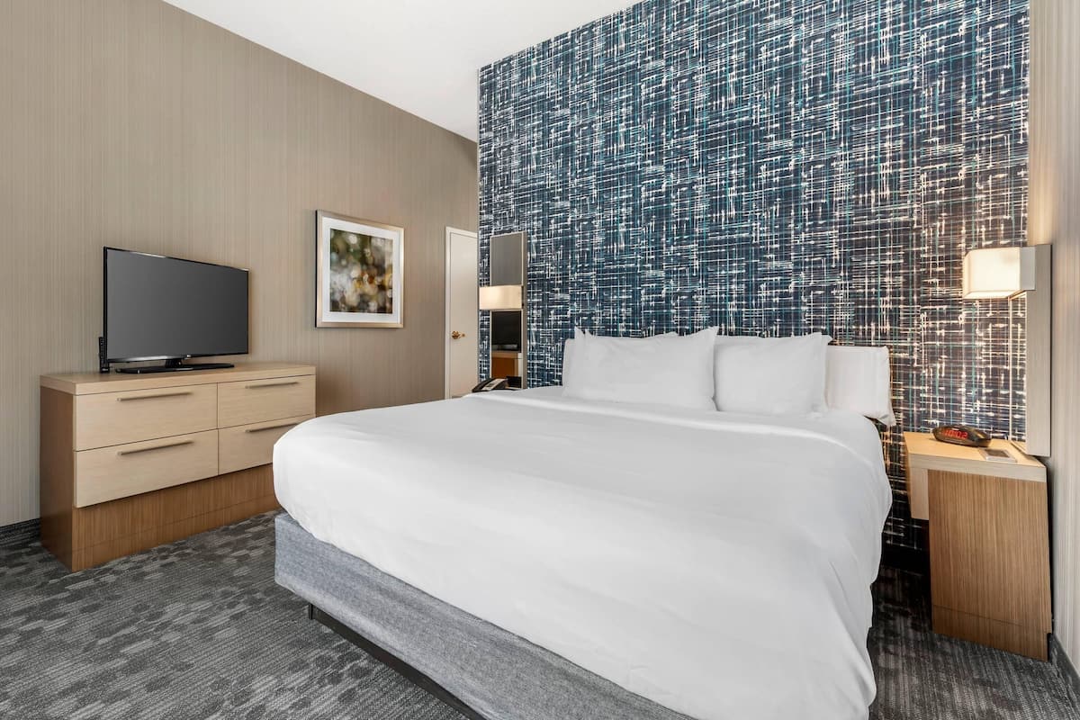 A hotel room with a large bed, a flat-screen TV, a nightstand, a wall-mounted lamp, and a mirror.