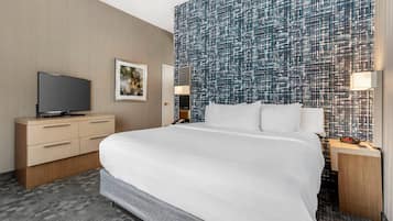 Una habitación de hotel con una cama grande, un televisor de pantalla plana, una mesita de noche, una lámpara de pared y un espejo.
