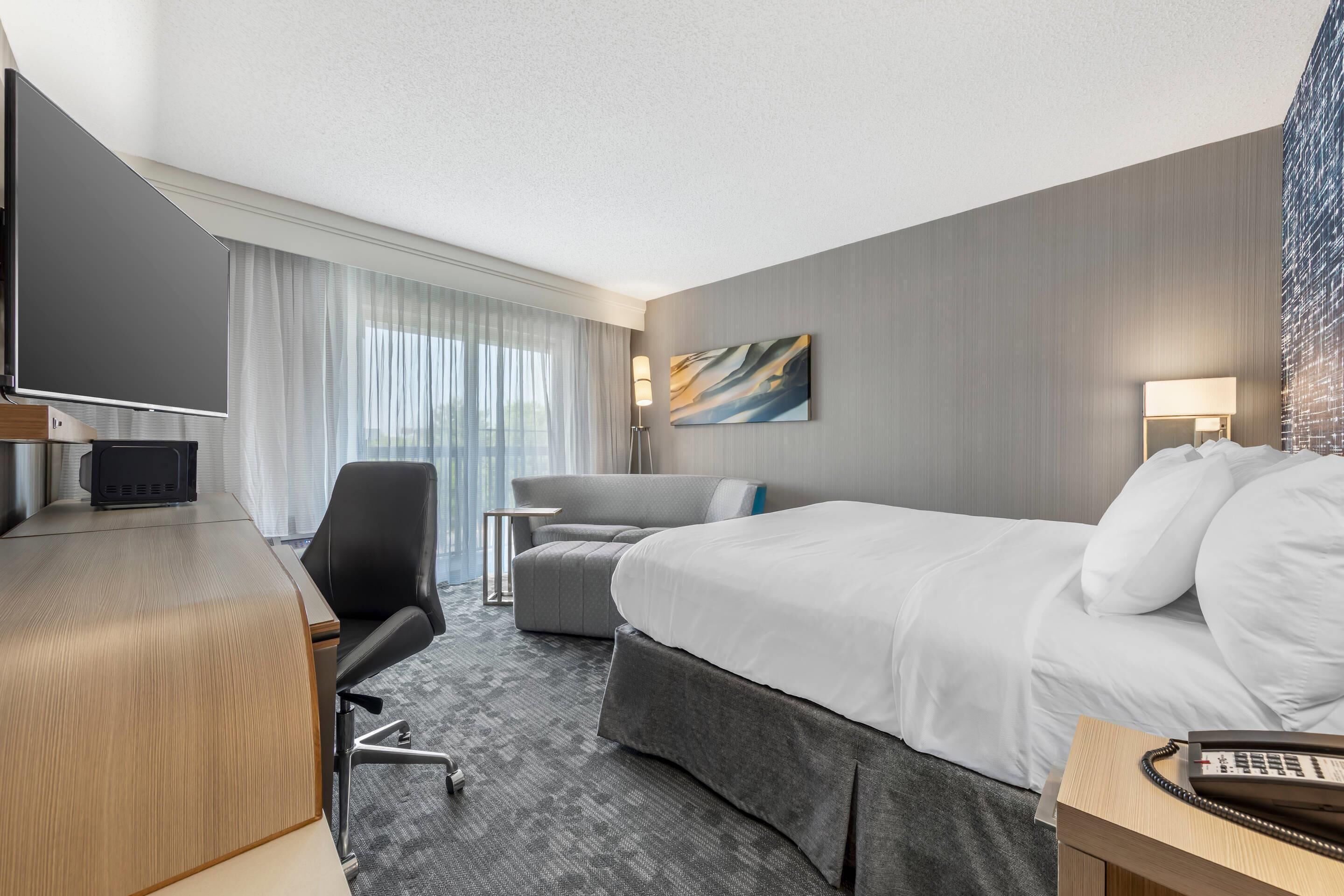 Une chambre d’hôtel équipée d’un lit, d’un bureau, d’une chaise, d’un téléviseur à écran plat et d’un tableau au mur.