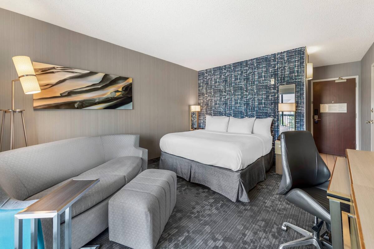 A hotel room with a bed, a sofa, a desk, and a chair.