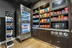 Un espace en libre-service comprenant des distributeurs de boissons réfrigérées, des étagères à collations, un four à micro-ondes et une balance.