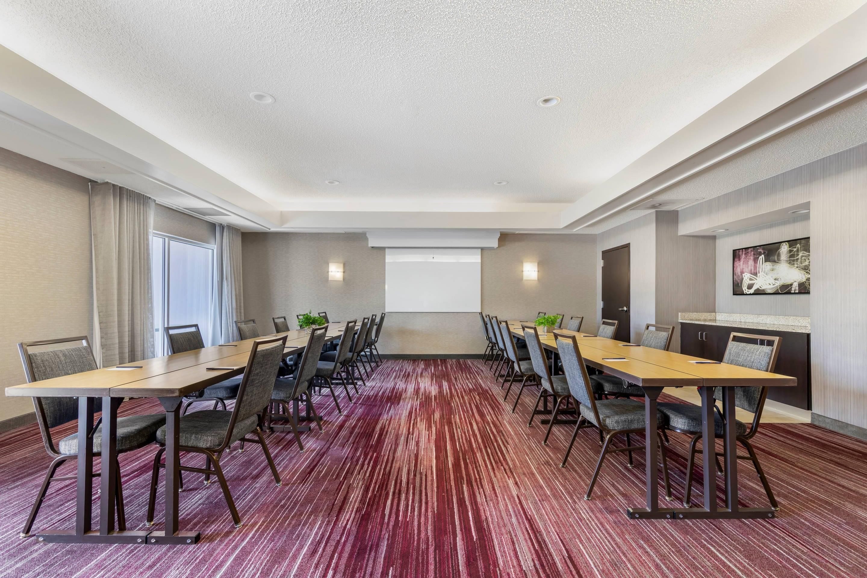 Une salle de conférence avec une longue table, des chaises, un écran de projection et un sol recouvert de moquette.
