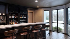 A bar area with a long counter, multiple stools, and a well-stocked liquor shelf. - Courtyard Houston The Woodlands (The Woodlands)