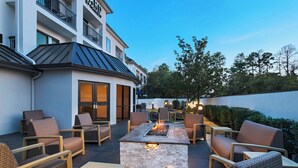 An outdoor patio with wicker furniture, a stone fire pit, and a view of a building with balconies. - Courtyard Houston The Woodlands (The Woodlands)