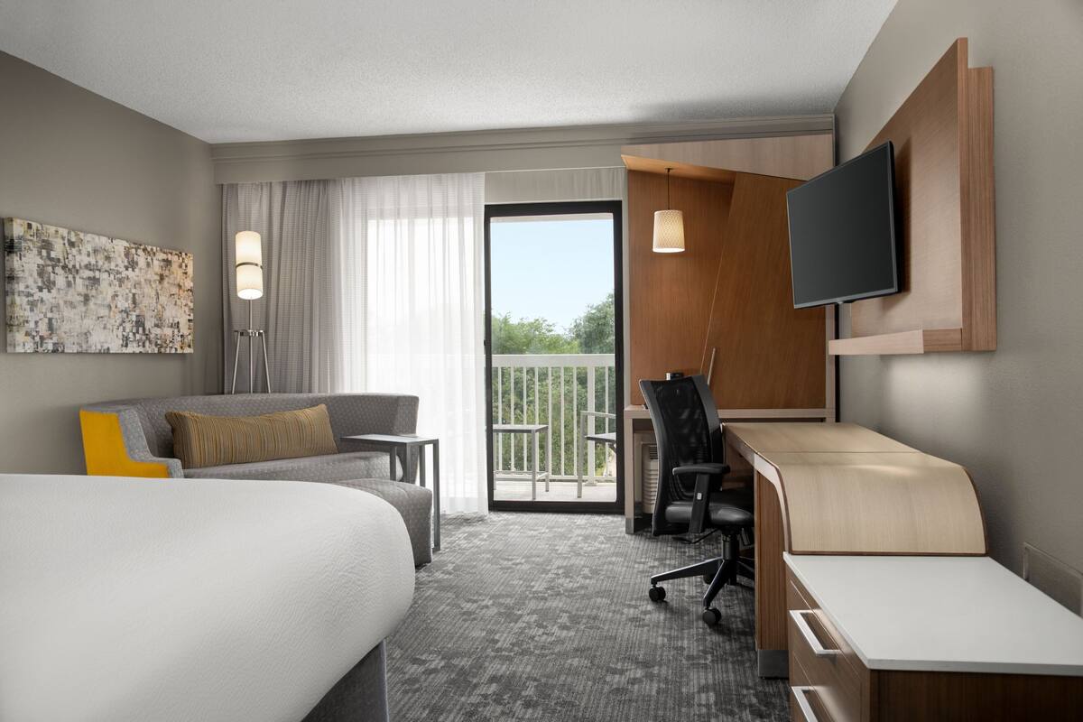 A hotel room with a bed, a desk, a chair, a television, and a balcony with a view.