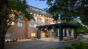 Um hotel Courtyard by Marriott com fachada moderna, entrada coberta e área de jardim bem cuidada.