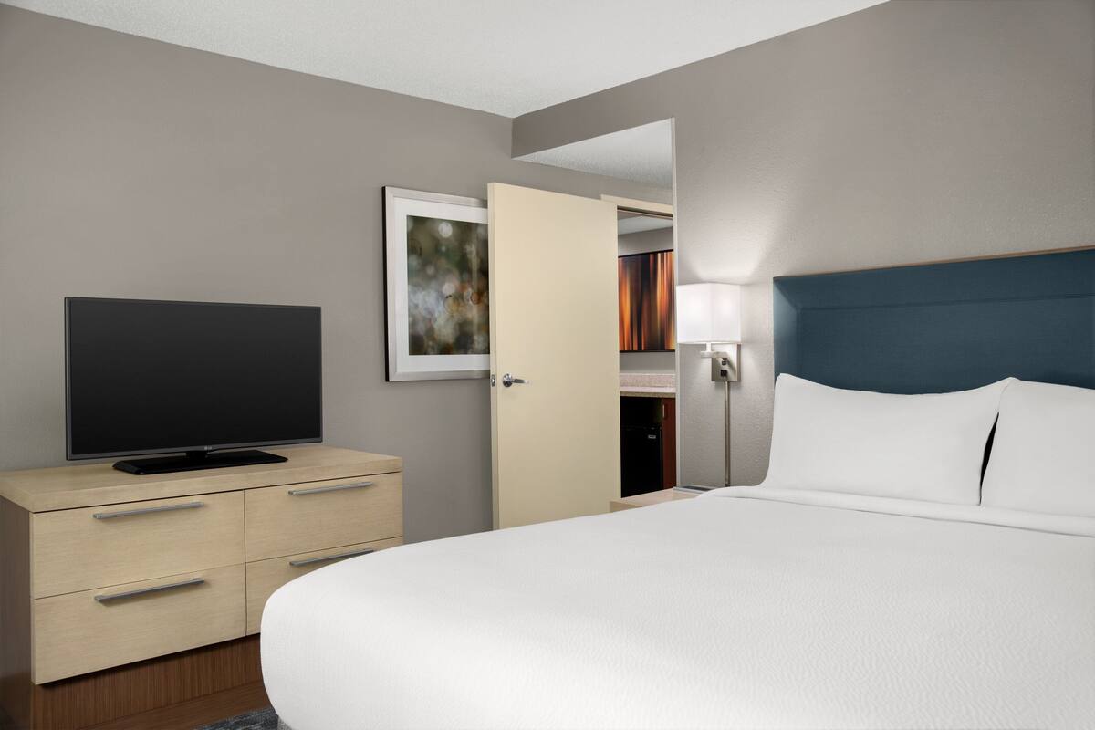 A hotel room with a bed, a TV on a dresser, a lamp, and a door leading to a closet.