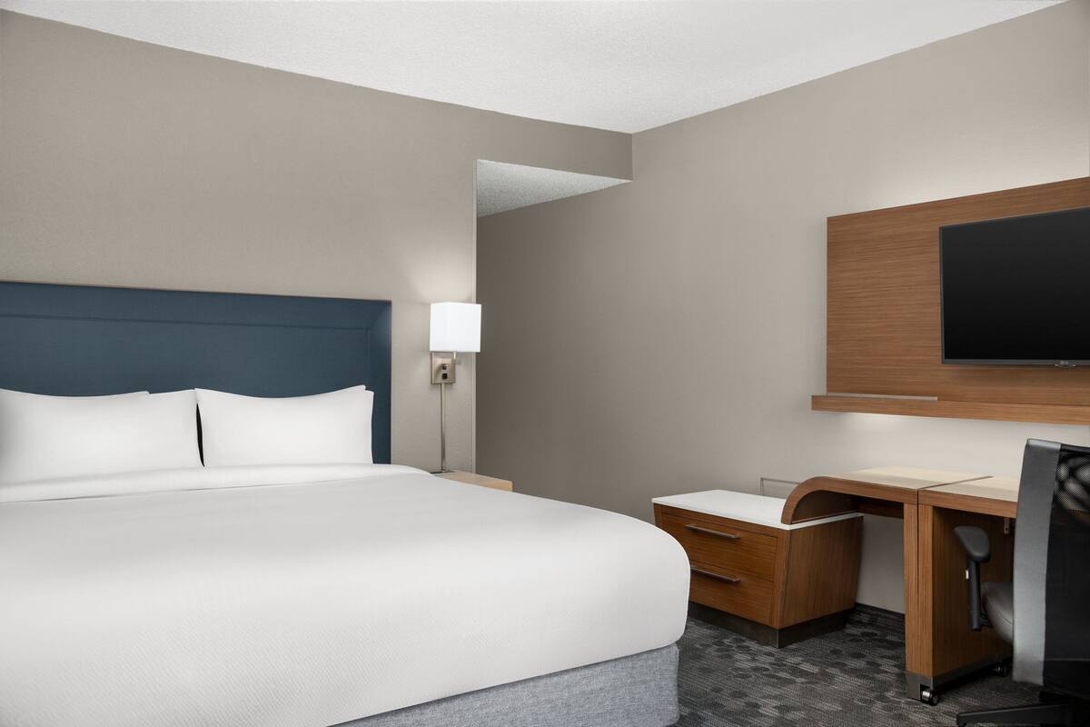A hotel room with a large bed, a desk, a chair, a flat-screen TV, and a nightstand.
